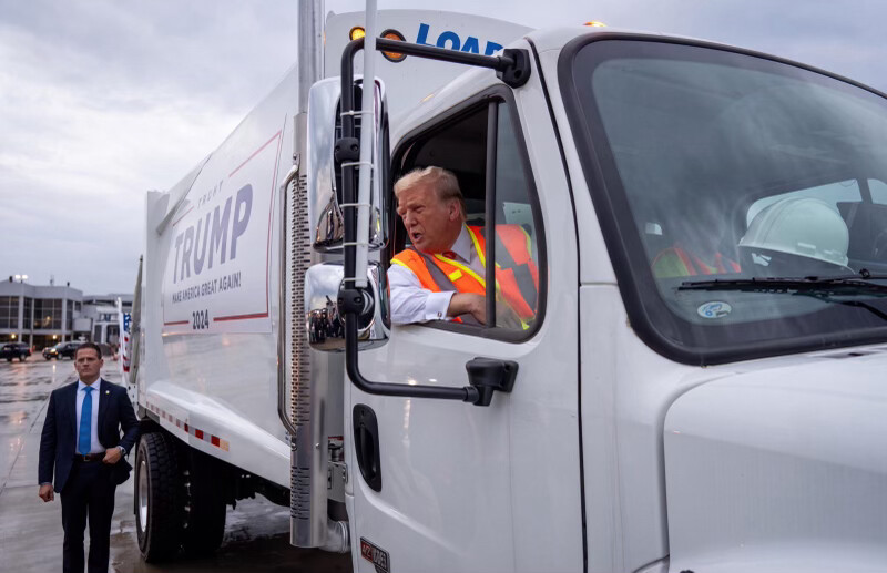 President Donald J. Trump leans out of a white garbage truck bearing 2024 campaign branding in Washington D.C.